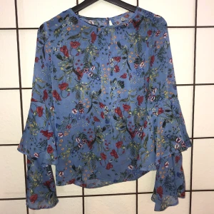 Blus med volangärmar  - Himmelsblå blus med blommor och volangärmar från dotti! Tunnare i tyget men inte särskilt genomskinlig, storlek UK8=S/36/38