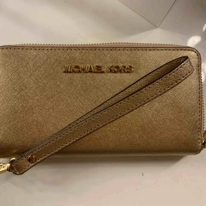  - Äkta Michael Kors plånbok i guld. Knappt använd, inga märkbara skador på plånboken.   Finns flertal fack i plånboken där (mindre) mobil, kort och kontanter får plats.   Säljer pga använder den inte. 