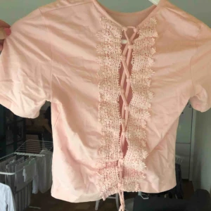  - En kort ljusrosa T-shirt med snör-broderi på ryggen. Köpt på HM för ca 100kr , använd 2-3 gånger. 