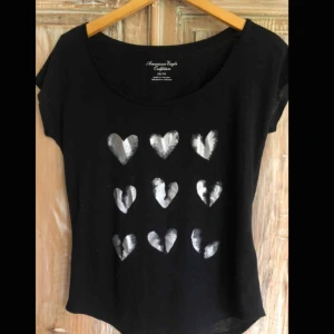  - Svart American Eagle t-shirt med silvriga hjärtprint. Står storlek XS i, men passar upp till M. Frakt ej inkluderat. 