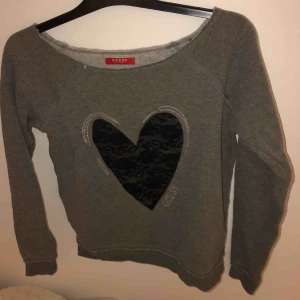  - Grå myströja från GUESS med svart spetshjärta på. Mjukt material inuti och lite större i halsen men snyggt att ha den lite nerhängande över ena axeln. Riktigt gott skick och nästan helt oanvänd 