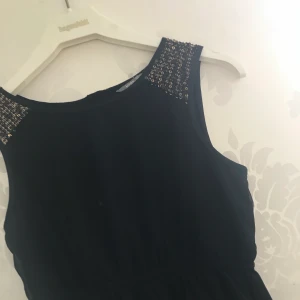 Klänning  - En jättefin svart klänning med guldiga biljetter vid axlarna. Ifrån kids (by Lindex) i storlek 152