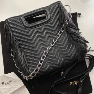 Maje väska - Superfin, trendig väska! Passar till allt! Svart med silverdetaljer. Den är använd, därav slitningar såsom att några ”fransar” ramlat av (inget som syns om man inte kollar noggrant). I övrigt är väskan fin och mycket användbar! (Nypris 2549kr -äkthetsbevis finns). Skickar gärna fler bilder! 