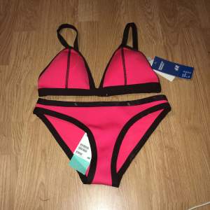 Neon röd/rosa bikiniset. Stängs baktill med knäppe. Fodrade kupor. Överdel strl 42, Underdel strl 36. Oanvänd, prislapp kvar och plomberad underdel.