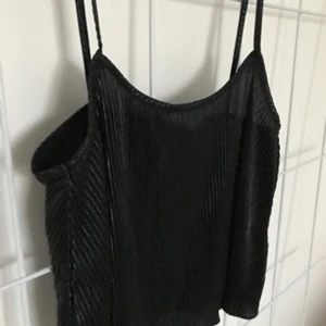  - Svart plisserad topp i glansigt tyg, passar en XS-M beroende på önskad passform. 