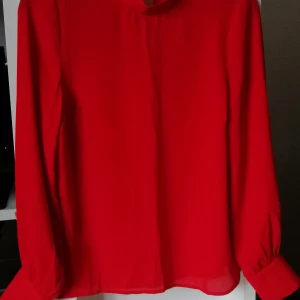 Röd blus från Gina Tricot, storlek 36 - Långärmad blus med slits i nacken under knäppningen. Finare tyg med lösare följsam passform. Snygg röd färg. Den knäpps även längst ute på ärmen och får ett mindre ballongutseende på underanrmana. Inköpt på Gina Tricot och använts 1 gång, Storlek 36. Nyskick. Hel och fläckfri. 