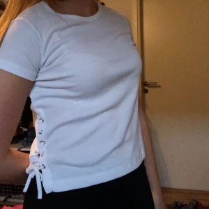 T-shirt med snörning - Vit ribbad gullig topp. Snörning på båda sidorna som man själv kan justera. Sitter jätteskönt. Storleken är 146/152 men är som XS-S. Nyskick. Kunden står för frakten eller möts i lund 💞