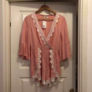 Somrig rosa jumpsuit med spetsdetaljer från H&M. Storlek 36/S, aldrig använd med prislapp kvar, nypris 299 kr. Perfekt för semester! 