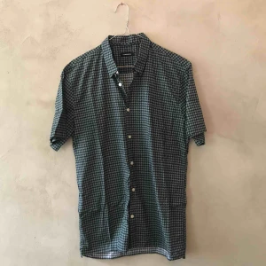  - Kortärmad skjorta i grönt och svart rutmönster. 