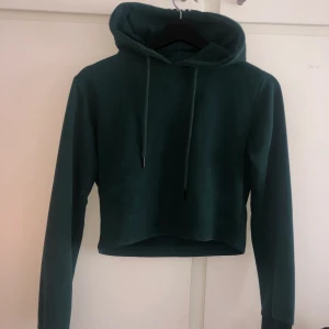 Croppad hoodie  - Mörkgrön croppad hoodie men ränder på luvan. Använd några få gånger, bra skick. Säljer då den är för liten för mig. Köparen står för frakt