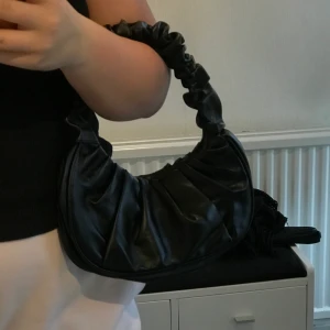 Axelväska - Väskan är sprillans ny! Utsidan är i fakeskinn och insodan vanligt tyg. Som man ser på bilden så stänger man den med en knapp. Lite tajt med att ha den precis vid axeln men kan också vara för att mina armar är lite större. Varför jag säljer denna är för att jag inte har någon nytta av den. KÖPAREN STÅR FÖR FRAKT