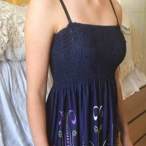  - Sommarklänning m smock runt bysten. Smala reglerbara axelband. Marinblå och mönster nertill i lilla, vitt, rosa o ljusgult. 