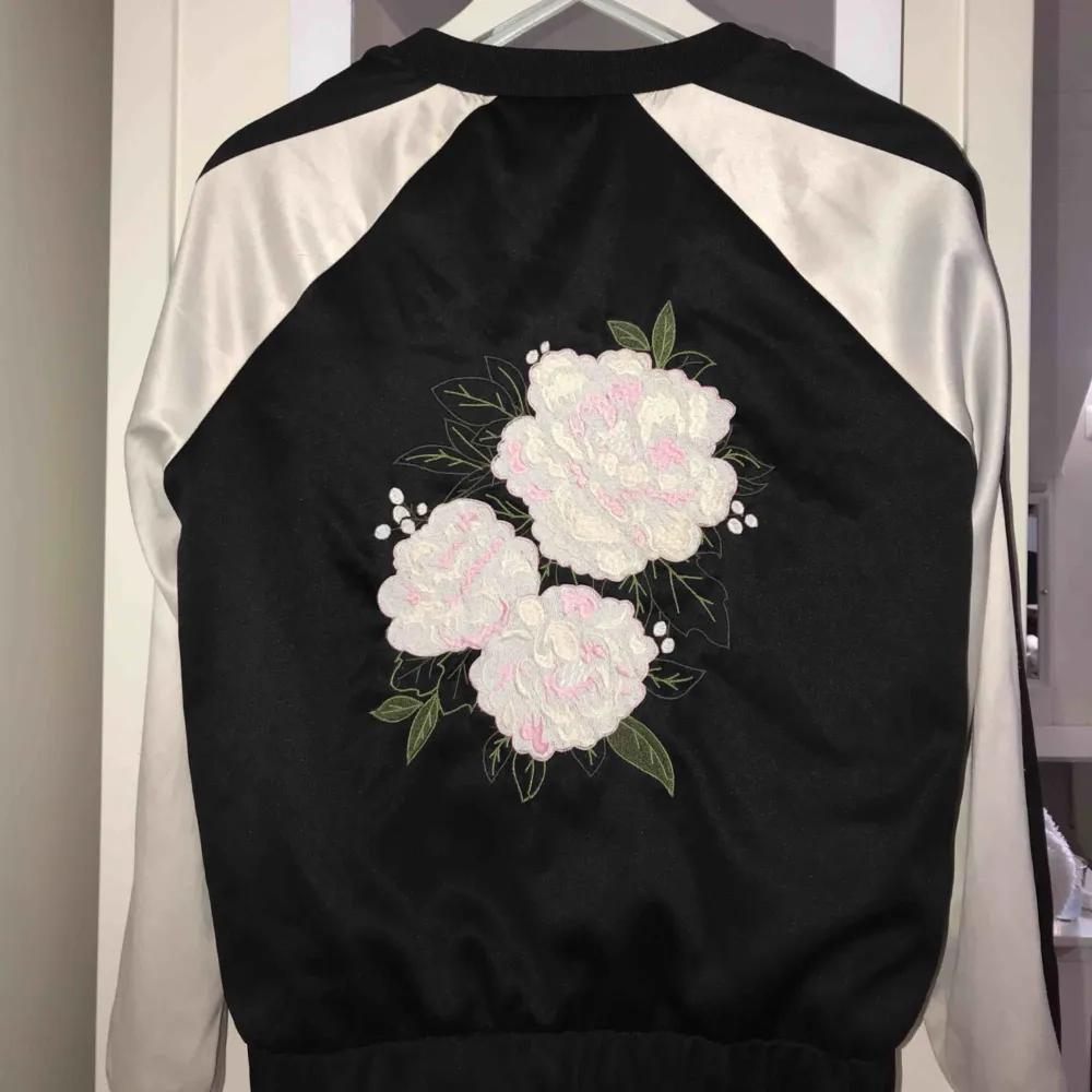 Svart vit tröja med dragkedja som öppning, samt ett blommigt broderat tryck på baksidan Ifrån Gina Tricot. Tröjor & Koftor.