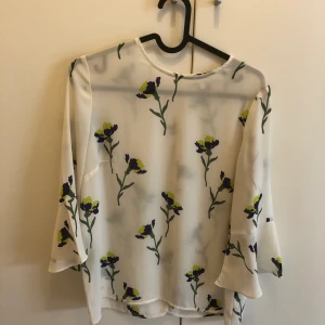 Blommig blus  - Figursydd blus med liten volang på änden av armarna. 