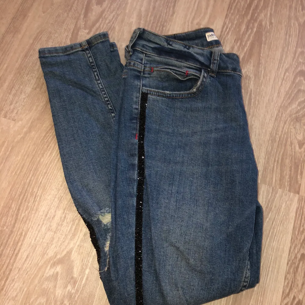 Blåa Zara jeans med slitningsdetaljer och glitterdetalj längst benen. Använda fåtal gånger och i mycket fint skick! Strl 38. . Jeans & Byxor.
