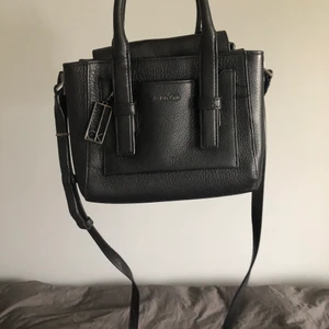 Calvine Klein väska  - Köpt i USA för 3 år sedan, nypris 1 900 kr. Gjord i läder och har två fack som är delade, samt ett fack i mitten med dragkedja. Fraktkostnad ingår inte i priset :)