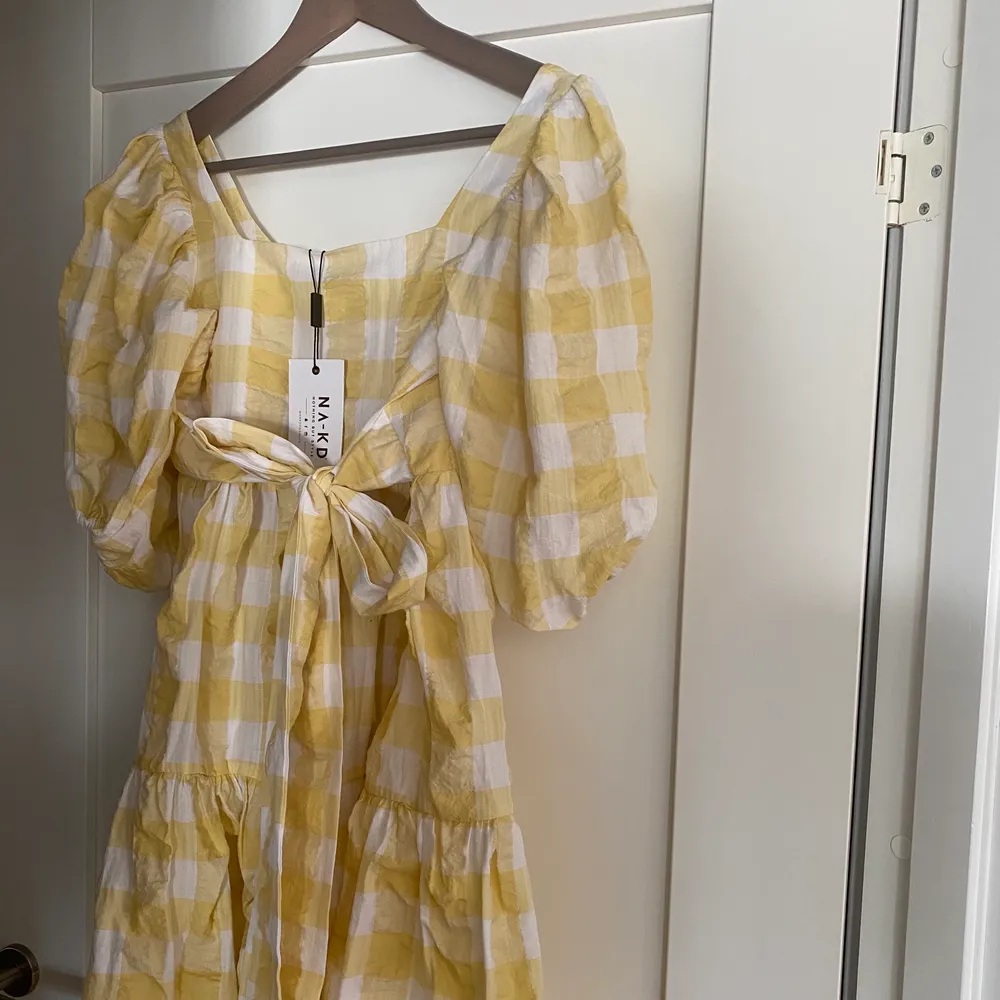 En gul rutig klänning med puffärm, helt ny med lapp kvar. Köpt för 599 kr. Köparen står för frakt . Klänningar.
