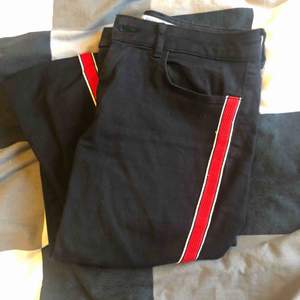 Svarta jeans med röd rand hela vägen utmed byxbenet på båda sidor. Använda fåtal gånger. Skönt stretch-tyg.