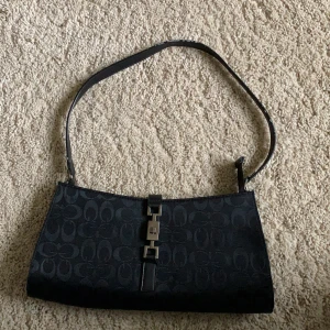 Svart baguettebag  - En medelstor svart baguettebag med silvriga spännen från okänt märke. Lite smått sliten i kanten av axelbandet och därav det lägre priset. Ett fint mönster i tyget av väskan. 75 kr + frakt men priset kan diskuteras 💞