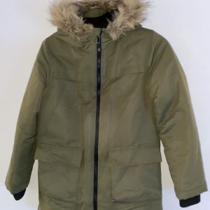 Vinterjacka med fejkpälsluva stl 152 - Snygg och varm, militärgrön vinterjacka i stl 152. Välanvänd men bra skick! Kommer från djur- och rökfritt hem. Frakt tillkommer!