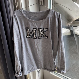 Grå tröja med glittrig text - Superfin grå tröja med knytning i midjan. Kommer från michael kors. Köpt på raglady i kungsbacka för 3 år sedan ungefär. Använd ett fåtal gånger, är i jättebra skick💕skriv till mig för mer infooo