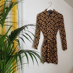Mönstrad skjortklänning, Monki, stl 36 - Mönstrad skjortklänning från Monki men fickor och skärp i midjan. Mörkt marinblå botten med senapsgula blommor och ljuslila detaljer. Stl 36 men lite liten i storleken. Noppig på sidorna. 100% viskos. Frakt tillkommer.