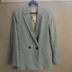 Ljusblå kavaj från H&M - En ljusblå kavaj från H&M. Köpt för 250kr.                     Nypris: 120kr +frakt. Storlek 34, normal i storlek.          Kavajen är aldrig använd, pris kan diskuteras vid snabb affär.     