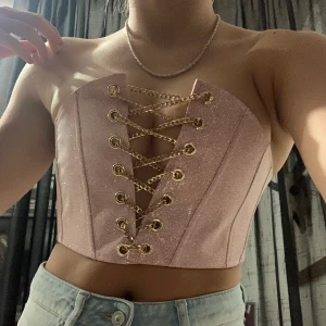 Korsett topp - Så cool korsett topp i rosa glitter och guldiga kedjor i fram. Aldrig använd och lappen är kvar. Den är från Poster Grl men är köpt på DollsKill där den är slut på sidan. Skitsnygg typ festival tröja!! Har tyvärr fått acceptera att den är för liten för mig och säljer därför. Den är liten i storleken så man kan inte ha så stora bröst tyvärr, men så snyggt med typ A/B kupa oså får man ett snyggt push! 