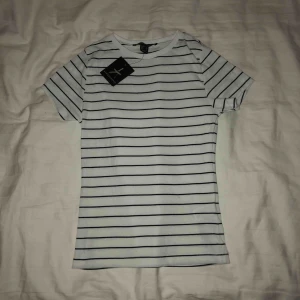  - Vit t-shirt med svarta ränder från Primark , aldrig använd bara testad, en liten blå tråd är på tröjan som man ser på bild nr 3, men är ingenting som syns mycket. (Köparen står för frakten)