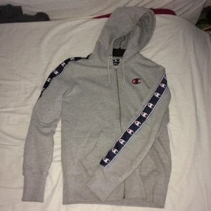 Champion Hoodie - Grå Champions hoodie. Knappt använd då den var mindre än önskat! Luvtröja med dragkedja. Storlek: XS Man. Priset är diskuterbart men värt enligt mig. Kontakta mig för mer info ifall du är intresserad!