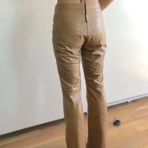  - Beiga läder byxor, lätt utsvängda nertill! Aningen för stora för personen på bilden så dom sitter tightare på en person som bär storlek 36, bra skick förutom en liten fläck på baksidan av höger ben som knappt syns när man har på sig dem