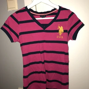  - Randig T-shirt från US POLO ASSN. Går i färgerna rosa med mörkblåa ränder. Använd fåtal gånger. Köparen står för frakten.