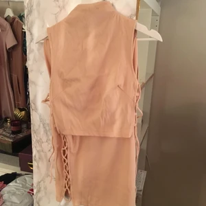  - Matchande set i ljusrosa/dusty pink. Oanvänd. Modellen är tight, och har snörning på sidorna. Toppen är crop top och kjolen har hög midja. Toppen är storlek 34, och kjolen storlek 36 