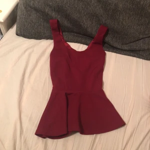  - Från Nelly. Snygg peplum topp i vinrött lätt ribbat tyg, och korsad i ryggsäljer pga den är förliten. Superbra skick då endast använd 1 gång. Köparen betalar frakt. Skriv för bättre bilder! 