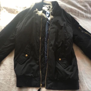  - Svart bomberjacka i längre modell, strl XS(stor i storleken). Blått foder och guldiga detaljer. Finns i Karlskrona, köparen står för eventuell frakt. Tar swish