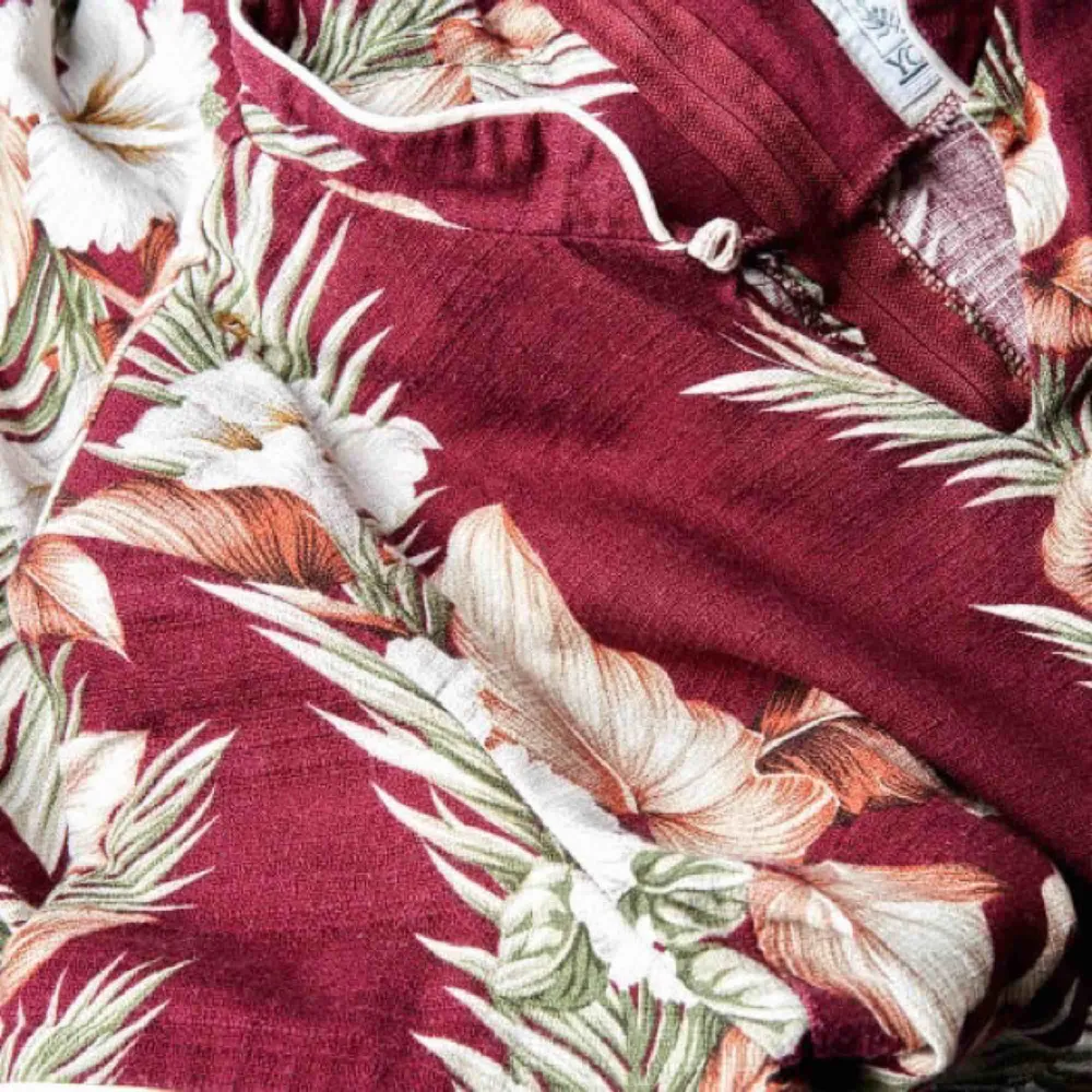 En hawaii-klänning med kinakrage. Slits i båda sidor, axelvaddar och vit passpoal runt ärm och krage. Mäter 116 cm från axel. . Klänningar.