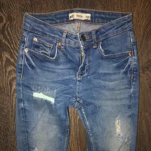 Ett par blåa slitna jeans som är i storlek 25 i midjan och 32 i längd, använda men ändå i bra skick.