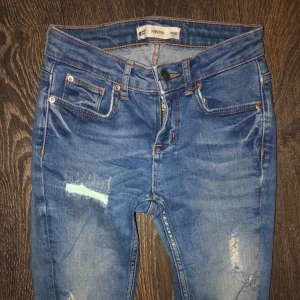  - Ett par blåa slitna jeans som är i storlek 25 i midjan och 32 i längd, använda men ändå i bra skick.