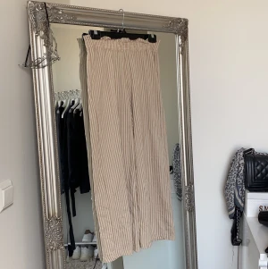 Vida croppade byxor  - Beiga vida byxor med vita ränder. Byxorna är i en croppad modell och slutar över ankel. Använda fåtal gånger men tre små hål och lite noppriga efter tvättning! Köparen står för frakten🥰