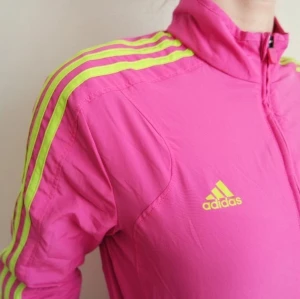 Neonrosa Adidas vindjacka, neon, vintage - Supersnygg neonrosa tunn Adidas vindjacka med gula stripes. Skicket på jackan är som nytt då den endast är använd ett fåtal gånger. Storlek 38. 200 kr, frakt ingår.