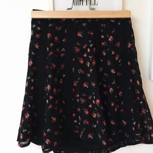 Svart kjol med hög midja från Gina Tricot. Knappt använd. Spetsdetaljer samt mönstrad med rosa/röda blommor. Resår där bak.