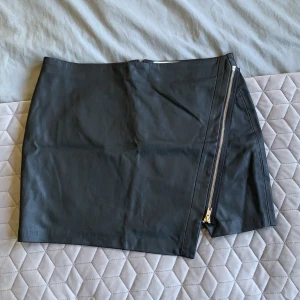 Svart skinnkjol från crocker  - Säljer denna coola skinnkjolen med silver detaljer ifrån crocker. Går även att öppna dragkedjan på framsidan för att få mer slit. Nyskick endast testad, säljer pga att den är för stor för mig!