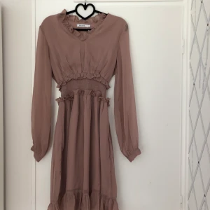 NA-KD klänning - Superfin rosa/mauve klänning från NA-KD. Endast använd vid ett tillfälle. Går ungefär till mitten av låret på mig som är 175 cm. Aningen stor i storleken, skulle säga att plagget snarare är en 36 än 34. Hör av er vid intresse!