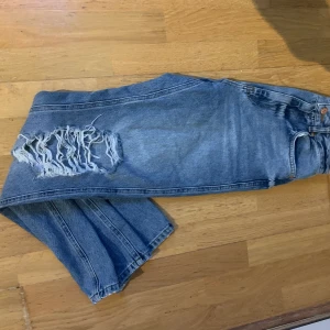 Blå jeans med Hål - NAKD Disstressed Straight Fit Jeans. Raka, Högmidjad jeans modell med hål på knäna. De är samma modell som  på modellbilden bara att detta är en ljusare färg. Denna färg är slut på hemsidan. Jeansen är i bra skick och säljes pga att dom är för små. Storlek 34. Frakt tillkommer