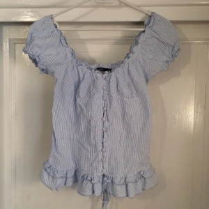  - Blå/vit-randig söt top från Atmosphere i storlek 10/38. Knappar hela vägen där fram och snörning i ryggen. Resor i "urringningen" och i ärmarna. Knappt använd!