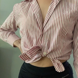 Randig skjorta  - 💗Så söt rosa o röd randig skjorta som antingen kan knäppas vanligt, knytas eller bära öppen. Bara använd ett par gången och är från märket Sand (broderat på sista bilden). Kan mötas i sthlm/Värmdö eller fraktas för 25 kr💗