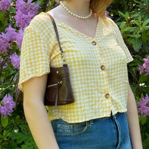 Topp med knappar - Säljer denna superfina topp med gult gingham mönster och knappar. Den är tunn i materialet vilket är såå skönt men ändå inte genomskinlig. Köpt förra sommaren men bara använd några enstaka gånger. 