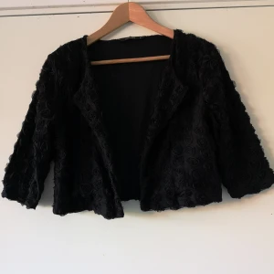 Cocktailjacka med påsydda rosor.  - Söt svart cocktailjacka med påsydda rosor. Knapp i kragen. Trekvartsärm. Från DUNNES. Står stl XL i den men jag är S/M och den passar bra på mig. Aldrig använd. 150 kr.