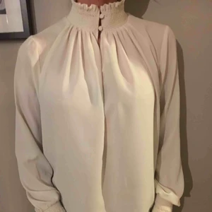  - Feminin cremevit blus med hög krage och fina detaljer. Begagnat skick