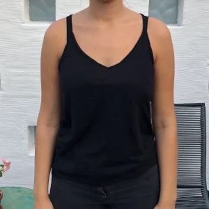 Sött svart linne med hål i ryggen stl. xs/s - Gulligt svart linne med hål i ryggen 😍 Toppen är stor i storleken och passar bättre en stl s (personen på bilden är en stl. s)